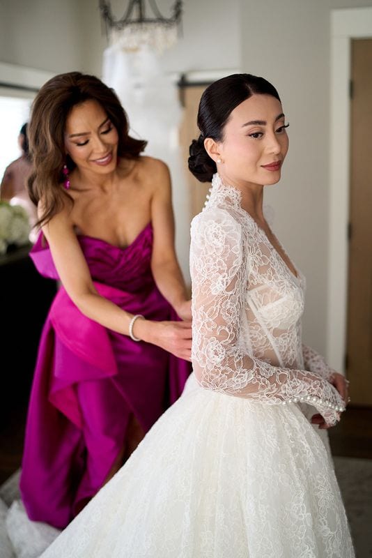 Her mother fastening the back of Noelle's lace dress