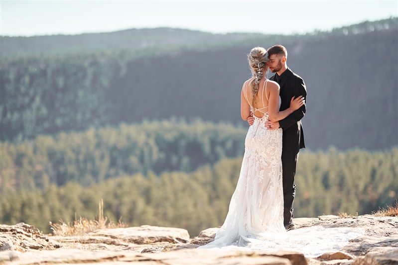 A couple on a rock ledge above a valley of pines