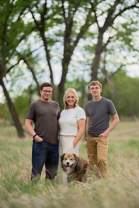 A mother, father, teenage son and their dog in tall grass under big cottonwood trees