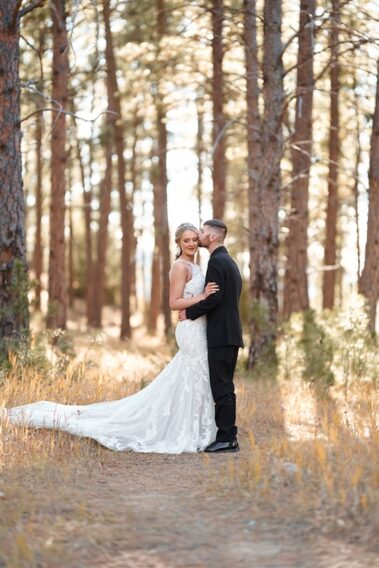 groom kissing bride on cheek in a forest, photographed for Complete Weddings & Events, black hills receptions wedding, photographer near me, black hills wedding, fall wedding
