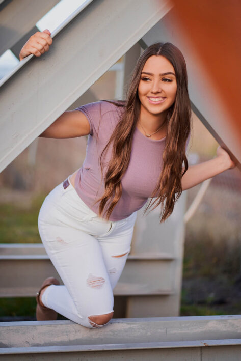 Senior girl with long hair smiling and climbing on a metal structure, rapid city senior photographer