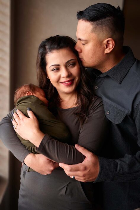 dad kissing mom on the head while she holds newborn baby, rapid city newborn photographer