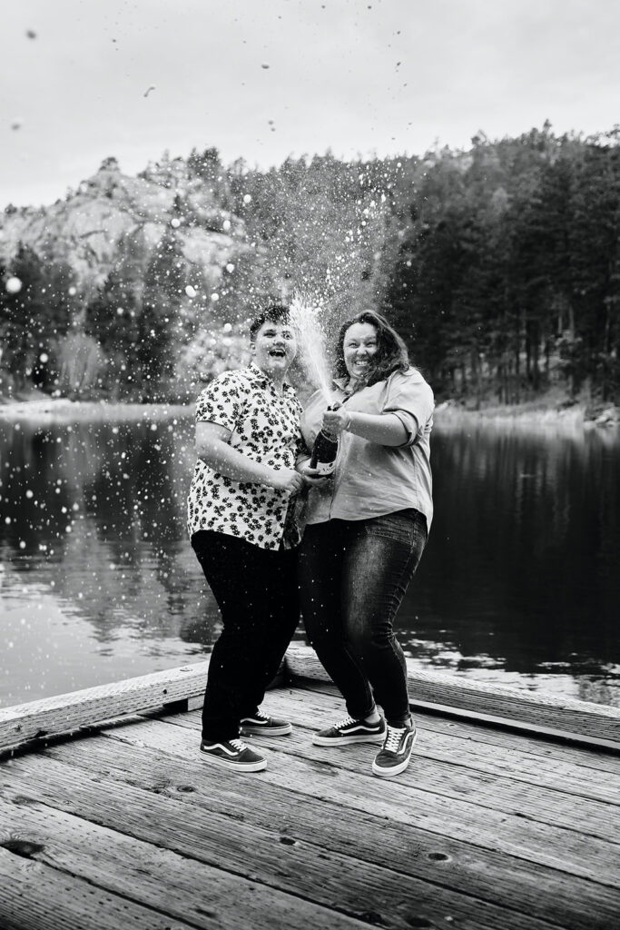 couple popping champagne on a dock, black hills engagement photos