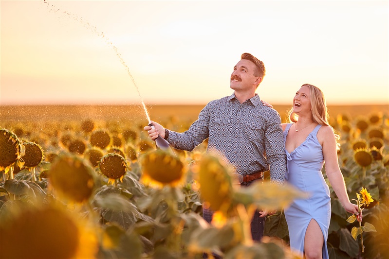 Photographed for Complete Weddings & Events, couple opening champagne, sunflower engagement session