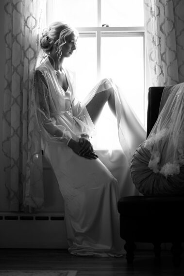 bride sitting on a window sill next to her veil